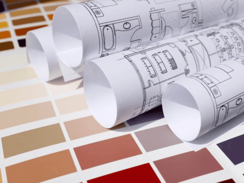 Rolled architectural blueprints on a color swatch chart with gradient beige to burgundy tones.