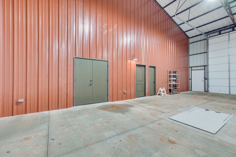 Unfinished barndominium shop interior with exposed red steel framing and a bare concrete slab