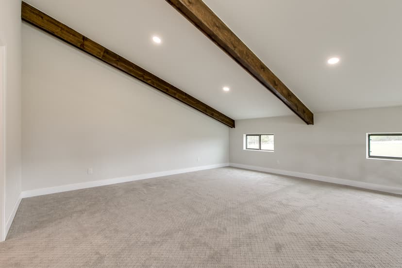 Open clear-span room in an Oklahoma barndominium with exposed stained timber beams and a sloped ceiling