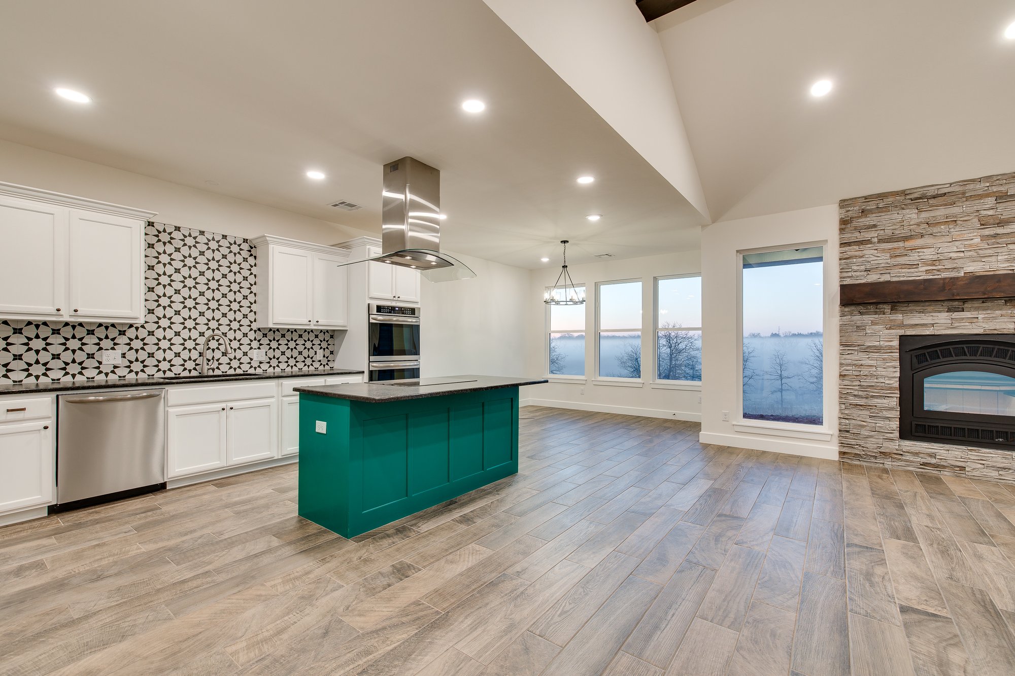 Open-concept kitchen and living room with stone fireplace by Noble Oklahoma custom home builder