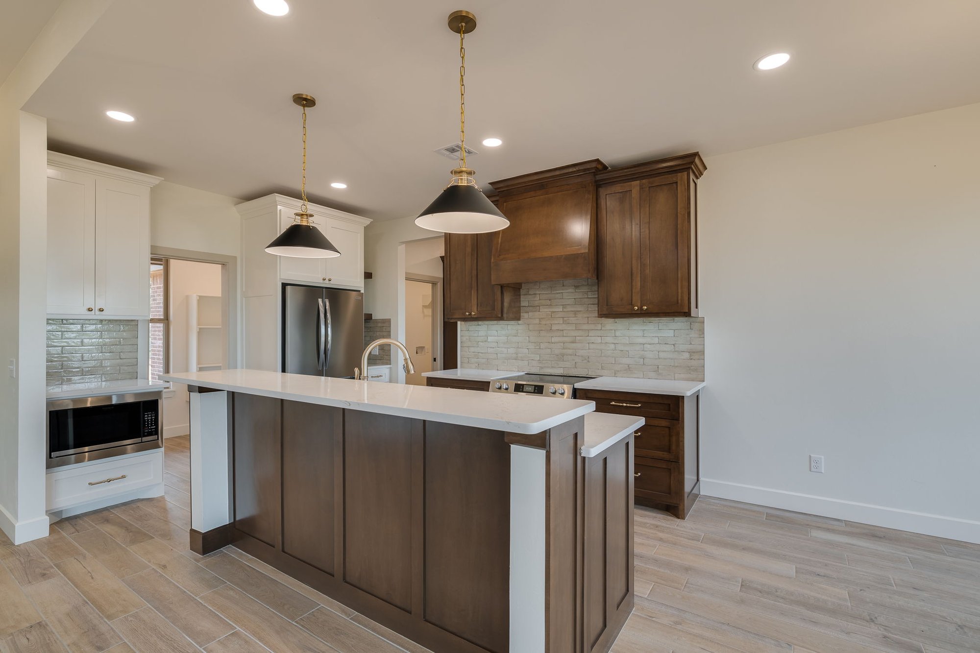 Modern kitchen in Minco, Oklahoma featuring warm wood cabinetry, quartz countertops, stainless steel appliances, and light wood-look tile flooring.