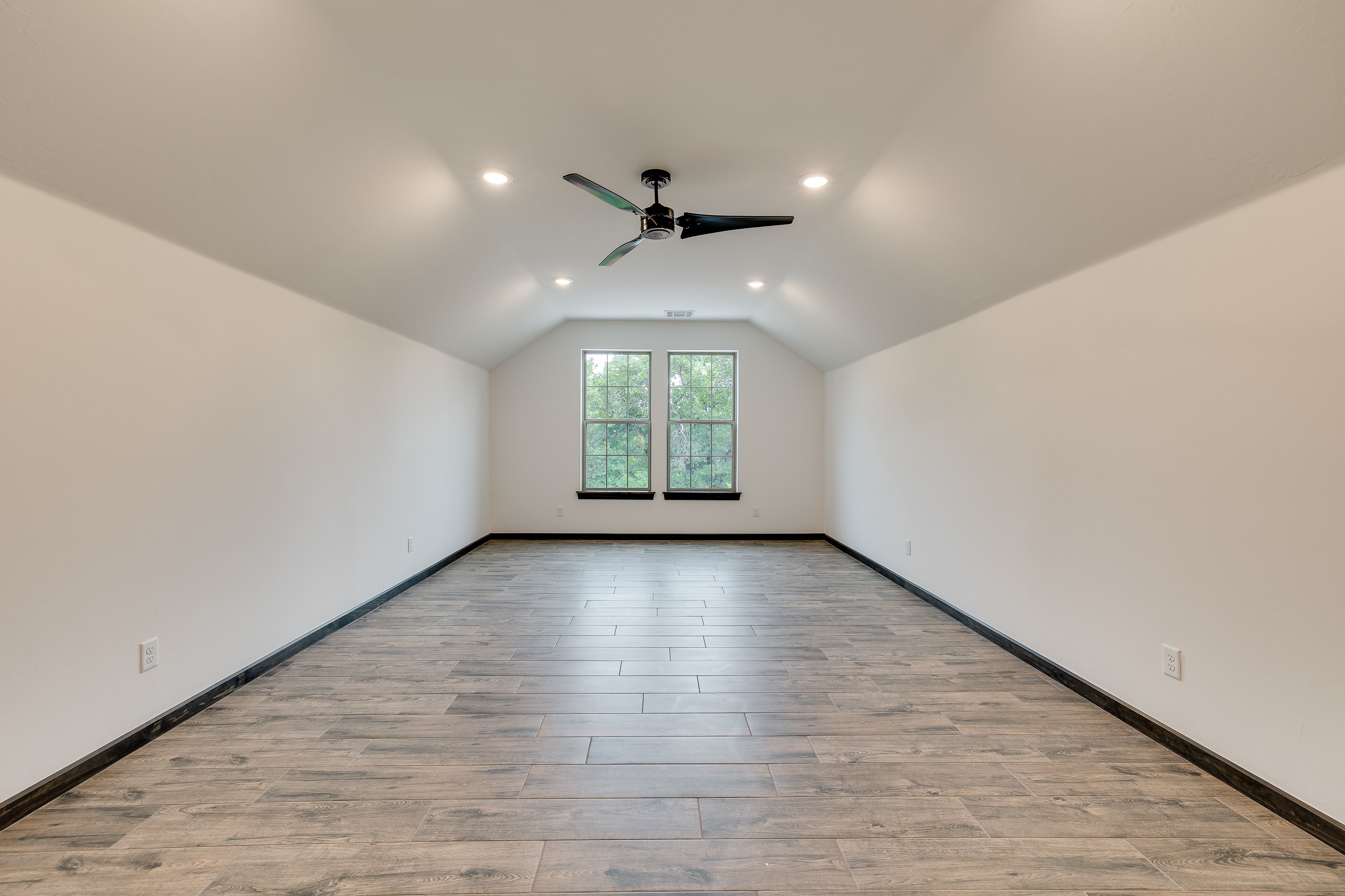Large bonus room with vaulted ceilings and wood-style flooring, demonstrating flexible design choices during the building process for extra living space in Norman, Oklahoma