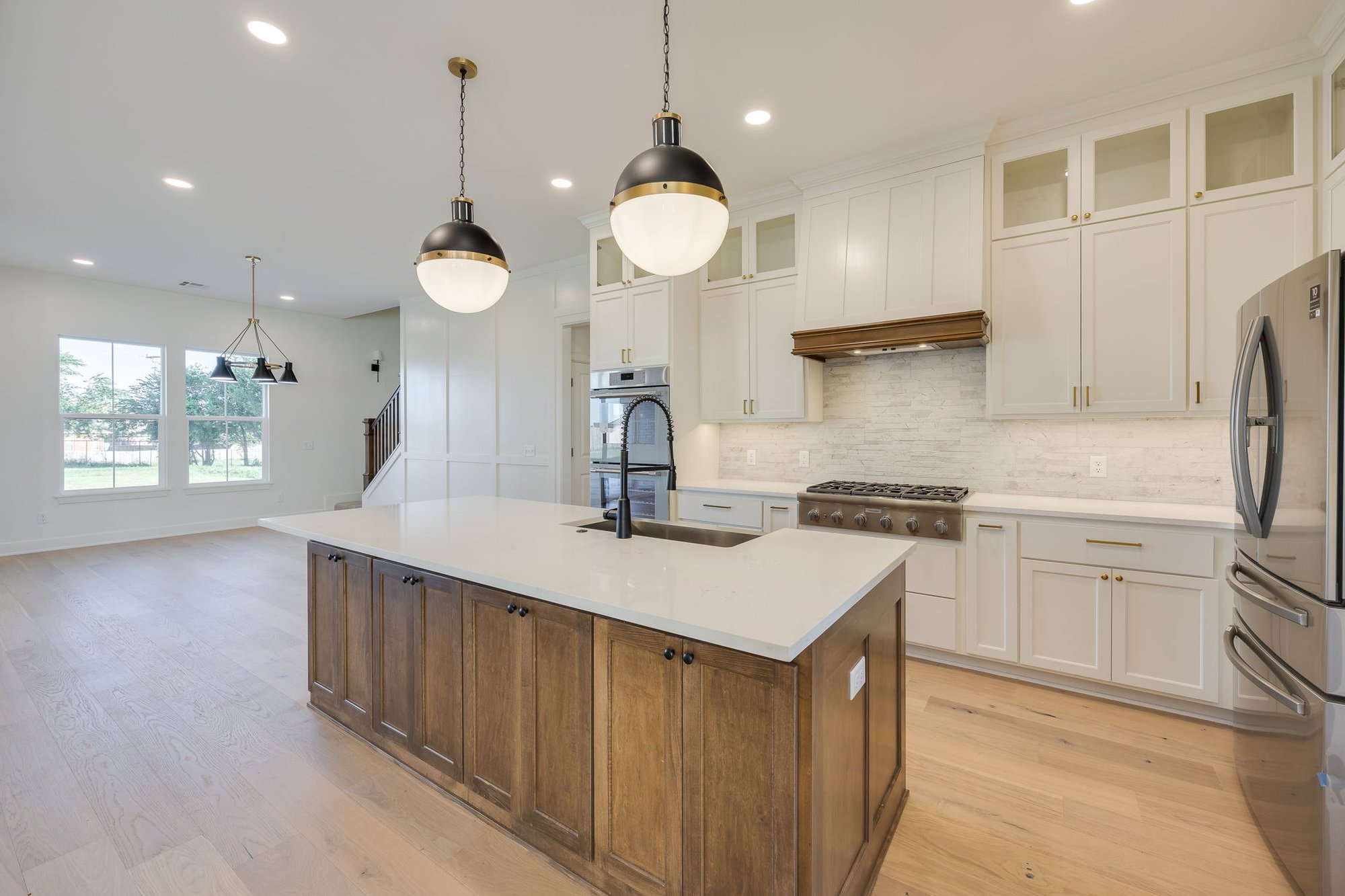 Elegant kitchen designed by a Yukon, Oklahoma custom home builder with a wood and white island, quartz countertops, pendant lighting, and white shaker cabinets.