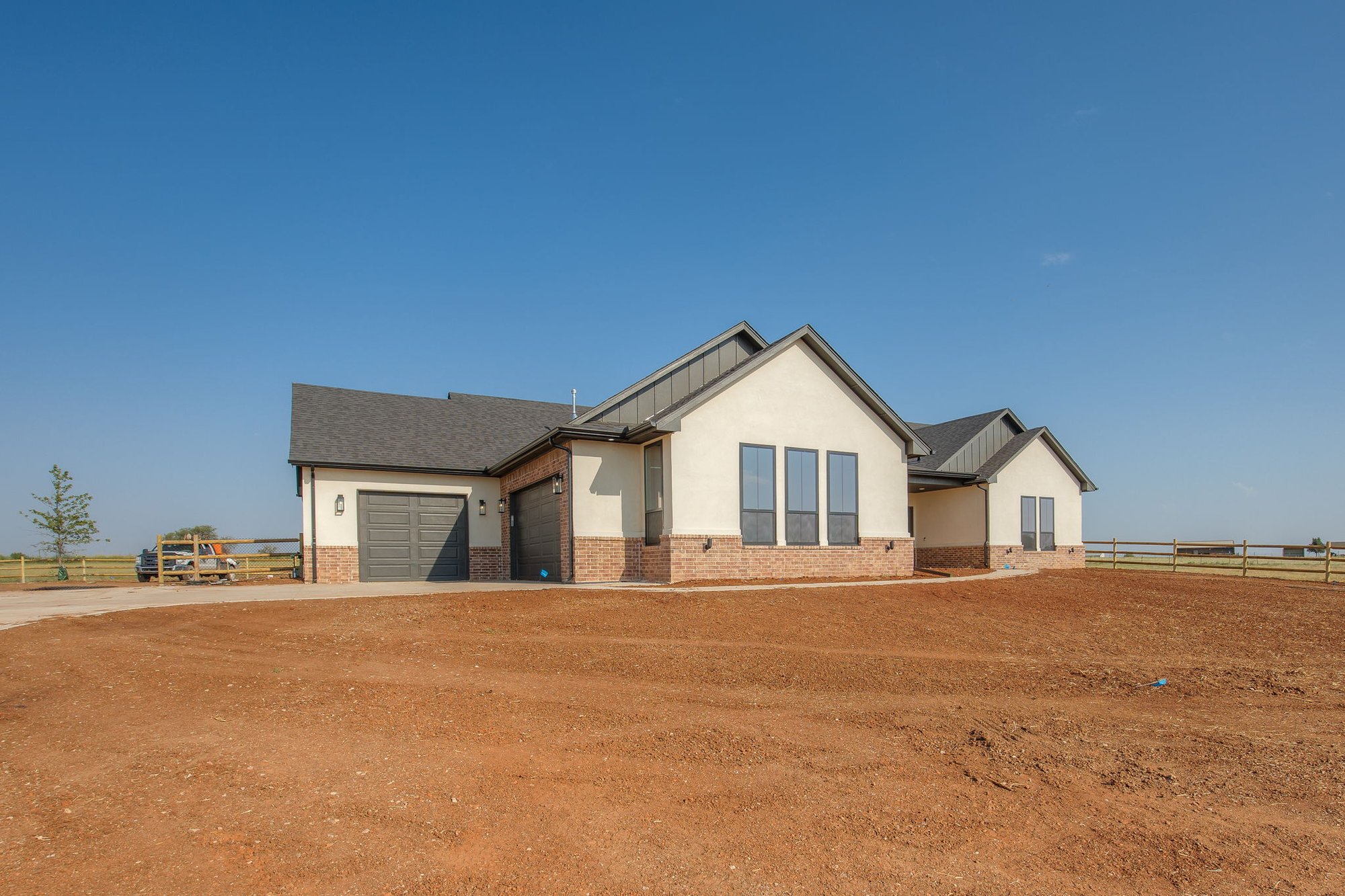 Exterior of a Piedmont, Oklahoma custom home with stucco and brick finish, gray garage doors, and large front-facing windows.