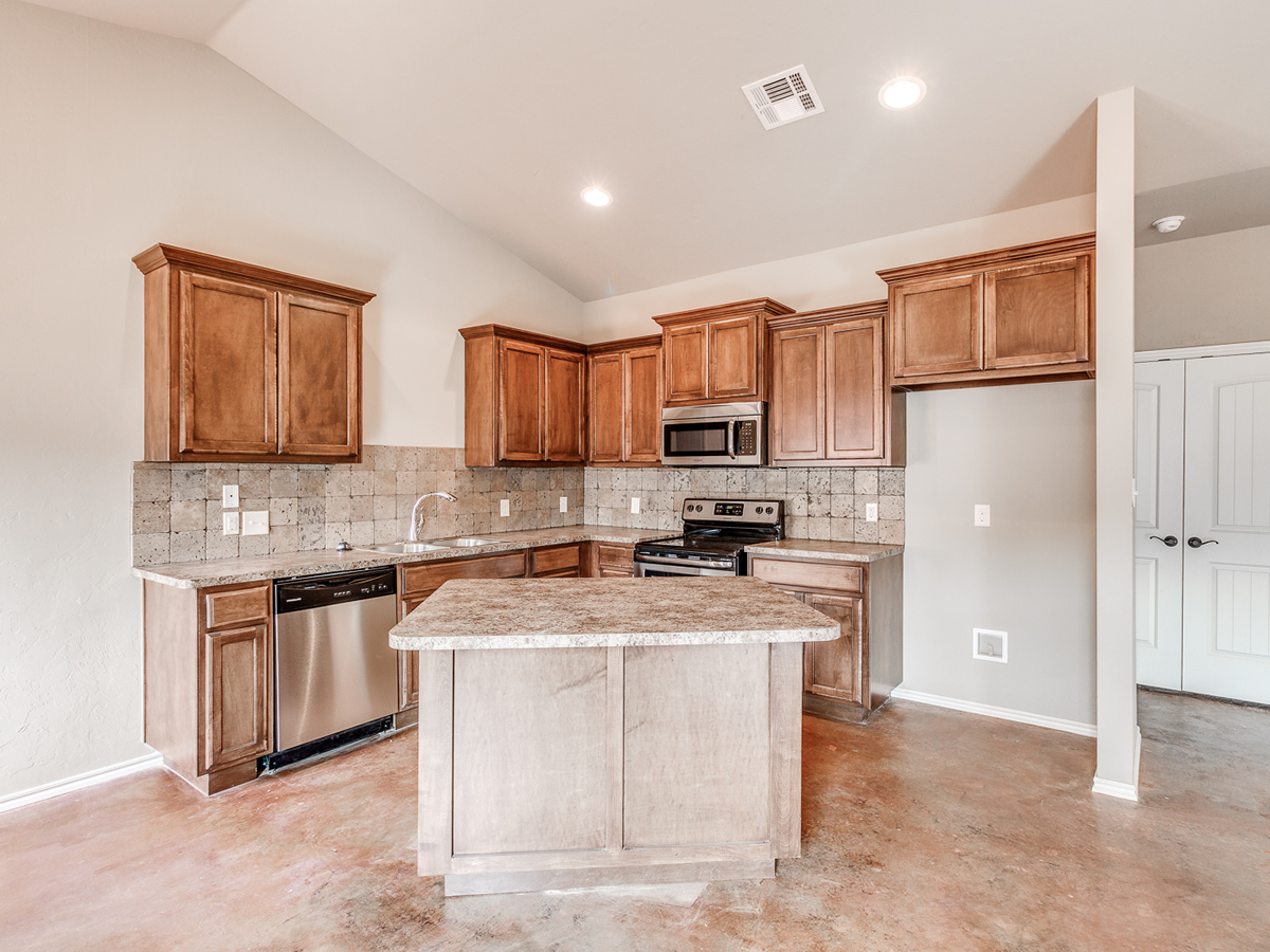 Warm-toned kitchen with tile backsplash and center island, showing a completed stage in the building process where finishes bring personality to the home.
