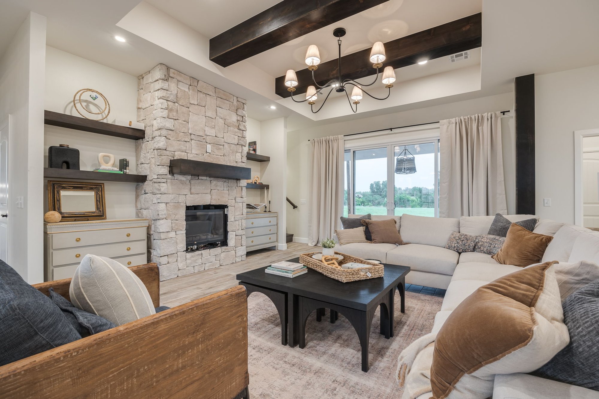 Custom farmhouse living room in Mustang, Oklahoma with stone fireplace, exposed wood beams, and a cozy sectional sofa, designed for family gatherings and modern comfort.