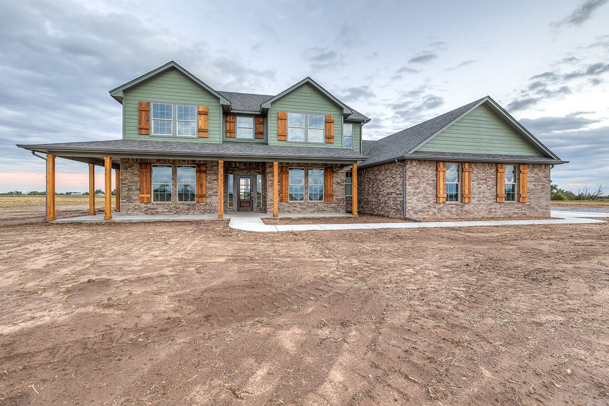 Custom two-story home in Oklahoma City with green siding, brick veneer, and cedar shutters showcasing a farmhouse-inspired exterior.