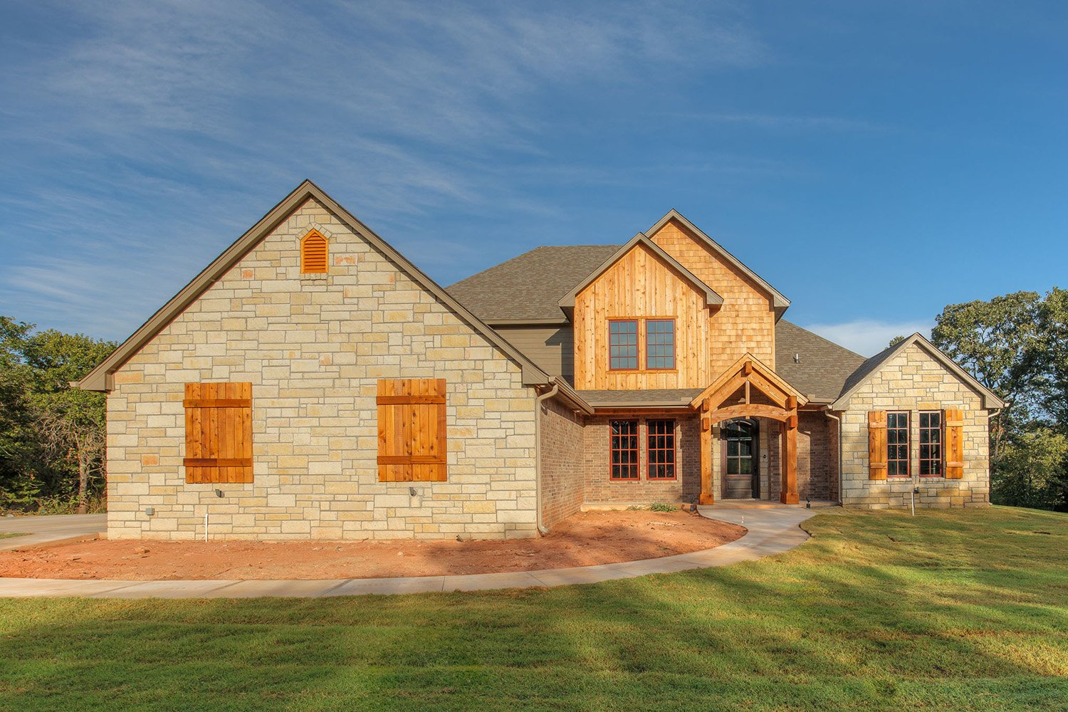 Elegant Oklahoma City two-story home with stone and wood siding, warm natural tones, and a gabled roof design.