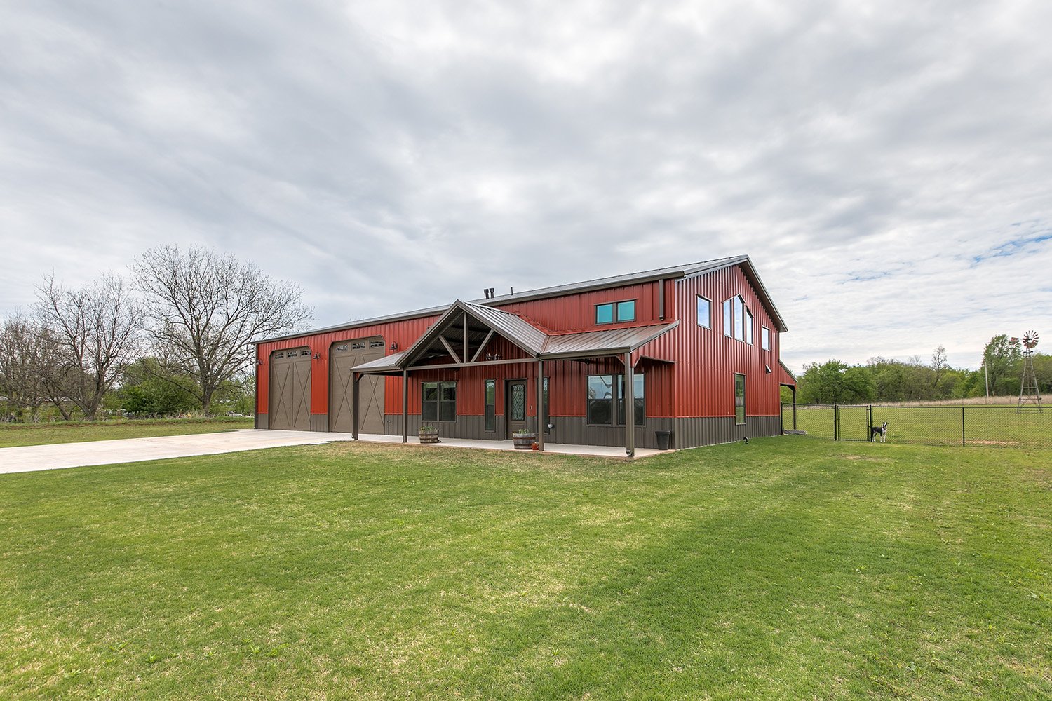 Modern barndominium in Oklahoma City featuring red steel siding, large barn-style doors, and a covered porch entry.