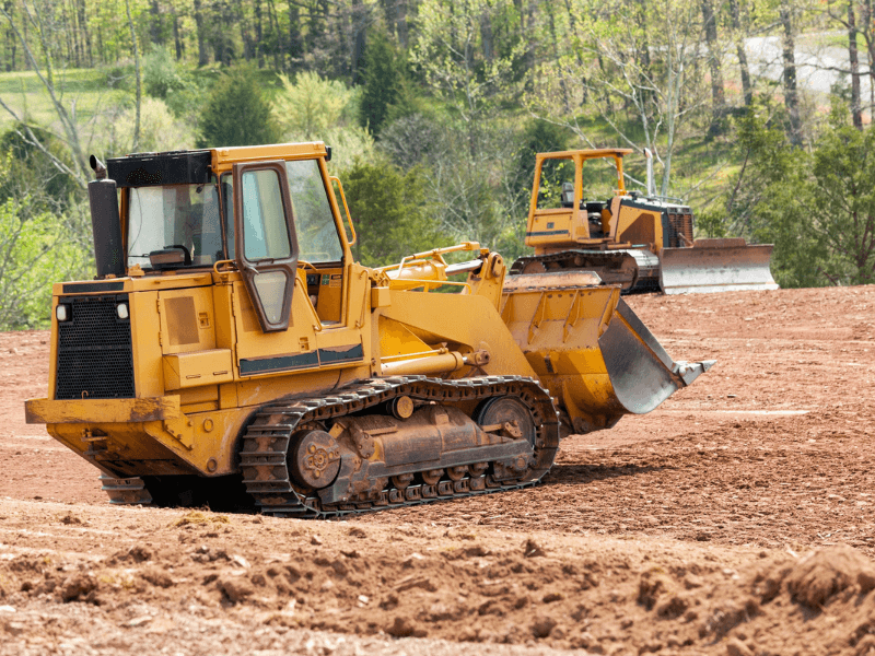 Two yellow bulldozers on a construction site with a forested background.