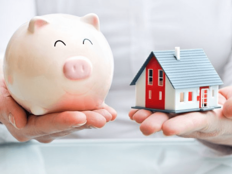 Hands holding a pink piggy bank and a small red and white model house.