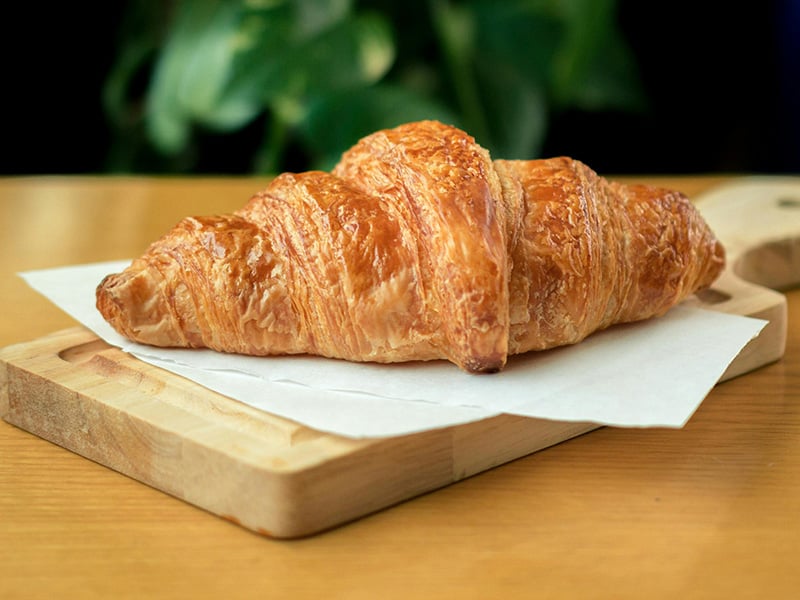 Freshly baked golden croissant on a wooden board at Just Baked Bakery in Yukon, Oklahoma.