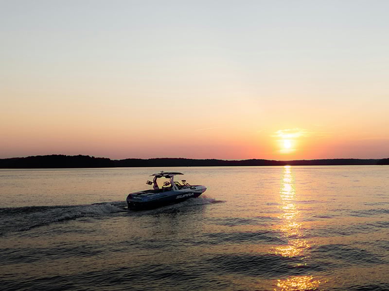 Scenic view of Lake El Reno in Oklahoma at sunset, with a speedboat gliding across the water and the sun reflecting on the lake’s surface.